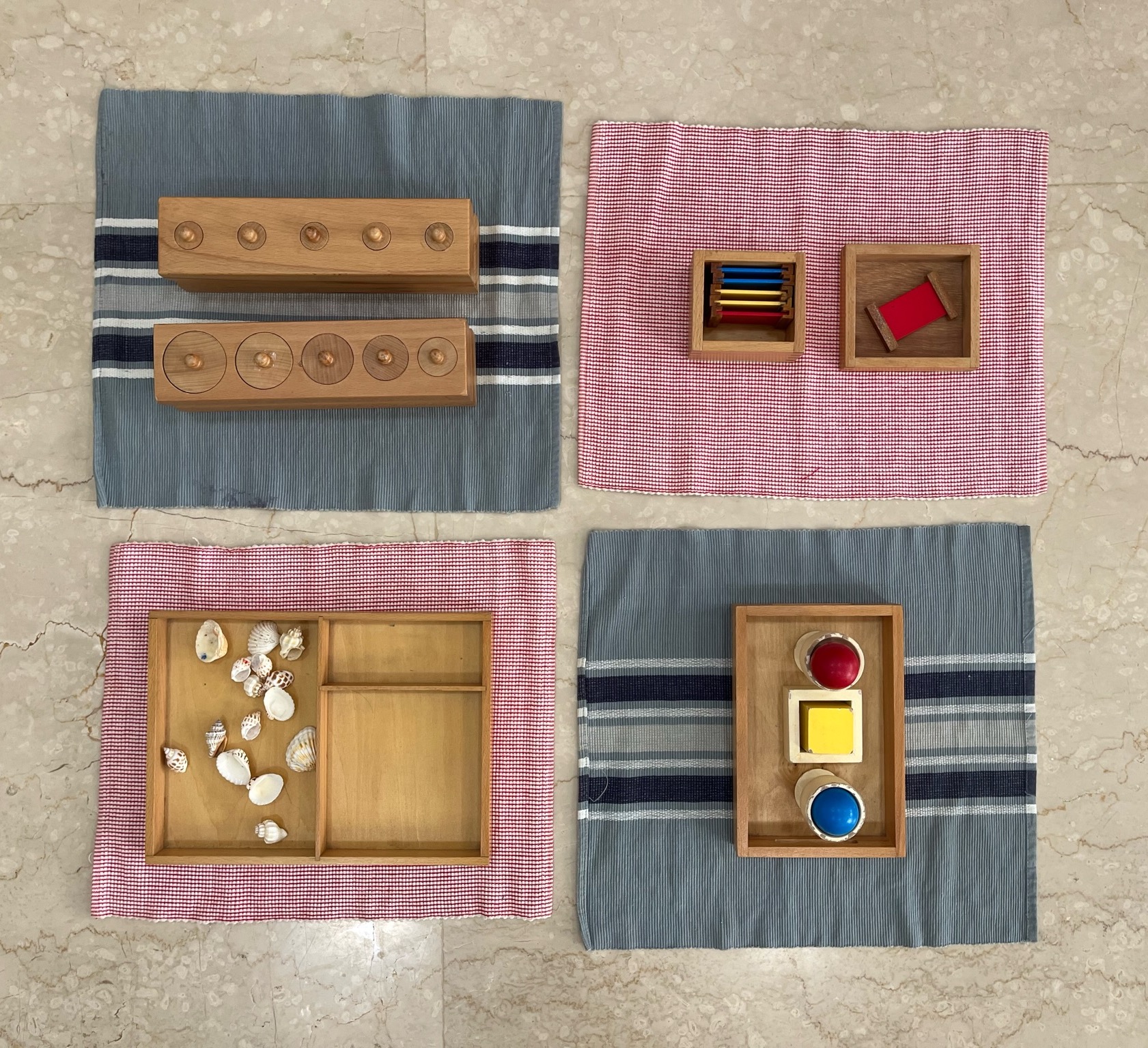 Montessori materials laid out on woven mats: knobbed cylinders, colour tablets, a shell-sorting tray, and colour balls
